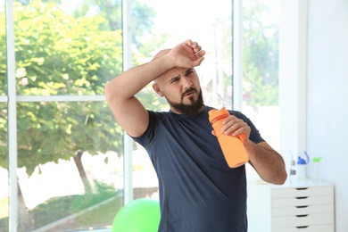 Photo of Tired overweight man with bottle of water in gym