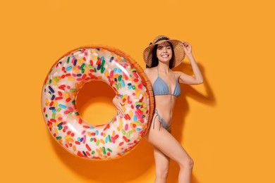 Young woman with straw hat holding inflatable ring against orange background