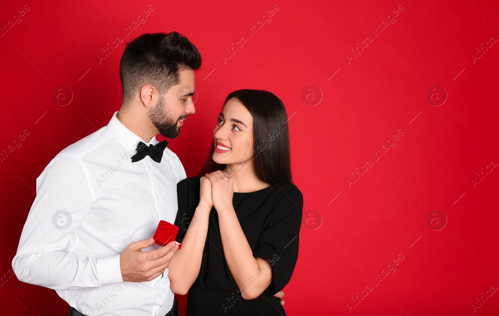 Photo of Man with engagement ring making marriage proposal to girlfriend on red background