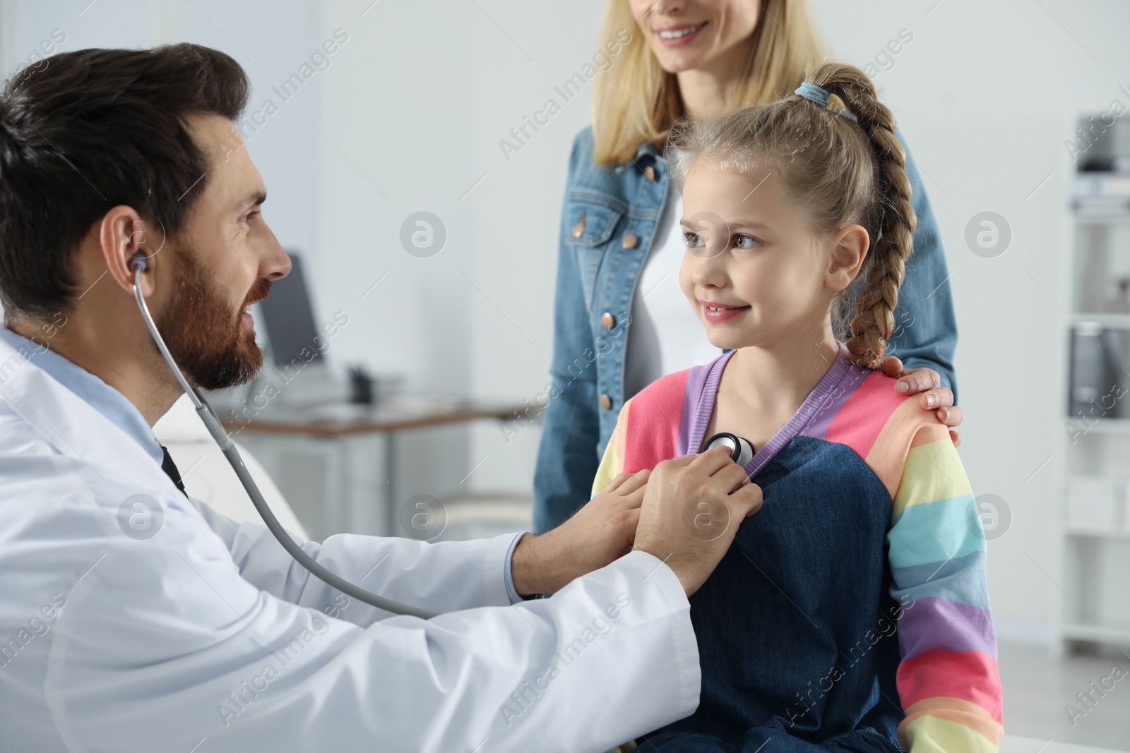 Photo of Mother and daughter having appointment with doctor. Pediatrician examining patient with stethoscope in clinic