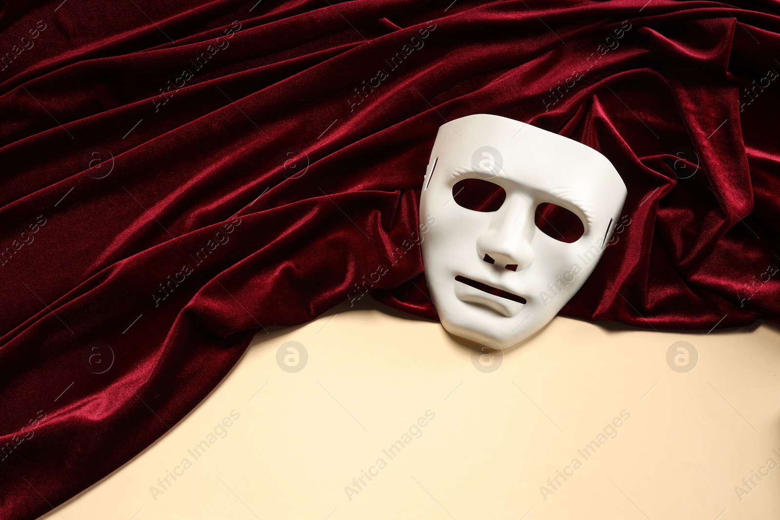 Photo of Theater arts. White mask and red fabric on beige background, above view