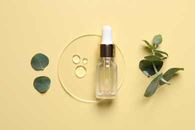 Photo of Bottle of cosmetic serum and green leaves on pale yellow background, flat lay
