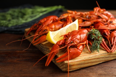 Delicious boiled crayfishes with lemon and dill on wooden table, closeup
