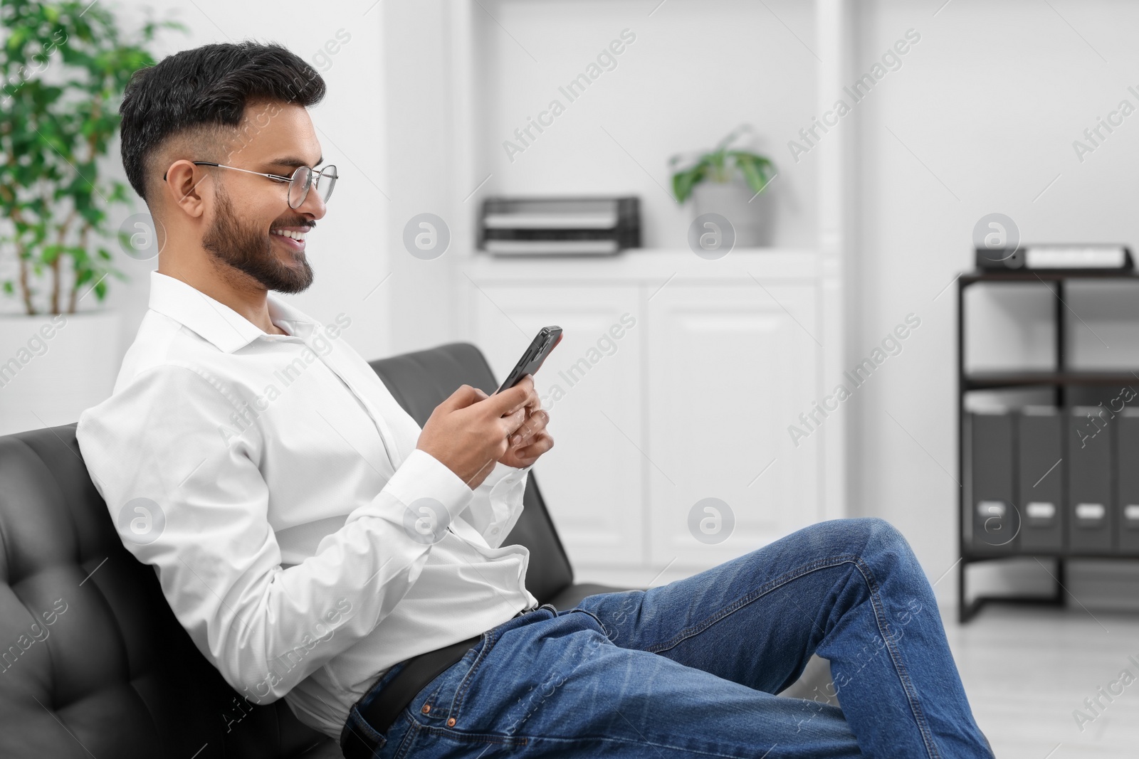 Photo of Handsome young man using smartphone on sofa in office