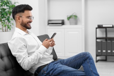 Handsome young man using smartphone on sofa in office