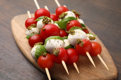 Photo of Caprese skewers with tomatoes, mozzarella balls, basil and pesto sauce on wooden table, closeup