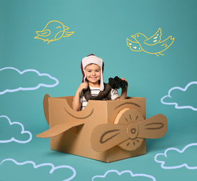 Cute little child playing in cardboard airplane on turquoise background with illustrations