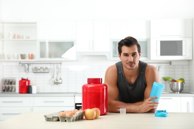Photo of Young athletic man with ingredients for protein shake in kitchen, space for text
