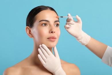 Doctor giving facial injection to young woman on light blue background, closeup. Cosmetic surgery