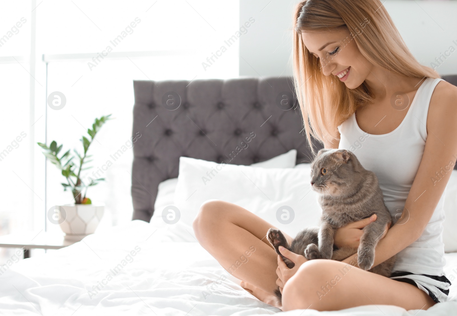 Photo of Young woman with her cute pet cat on bed at home