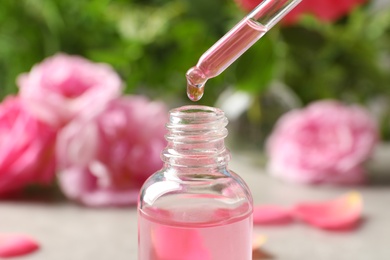 Photo of Dripping rose essential oil into bottle against blurred background