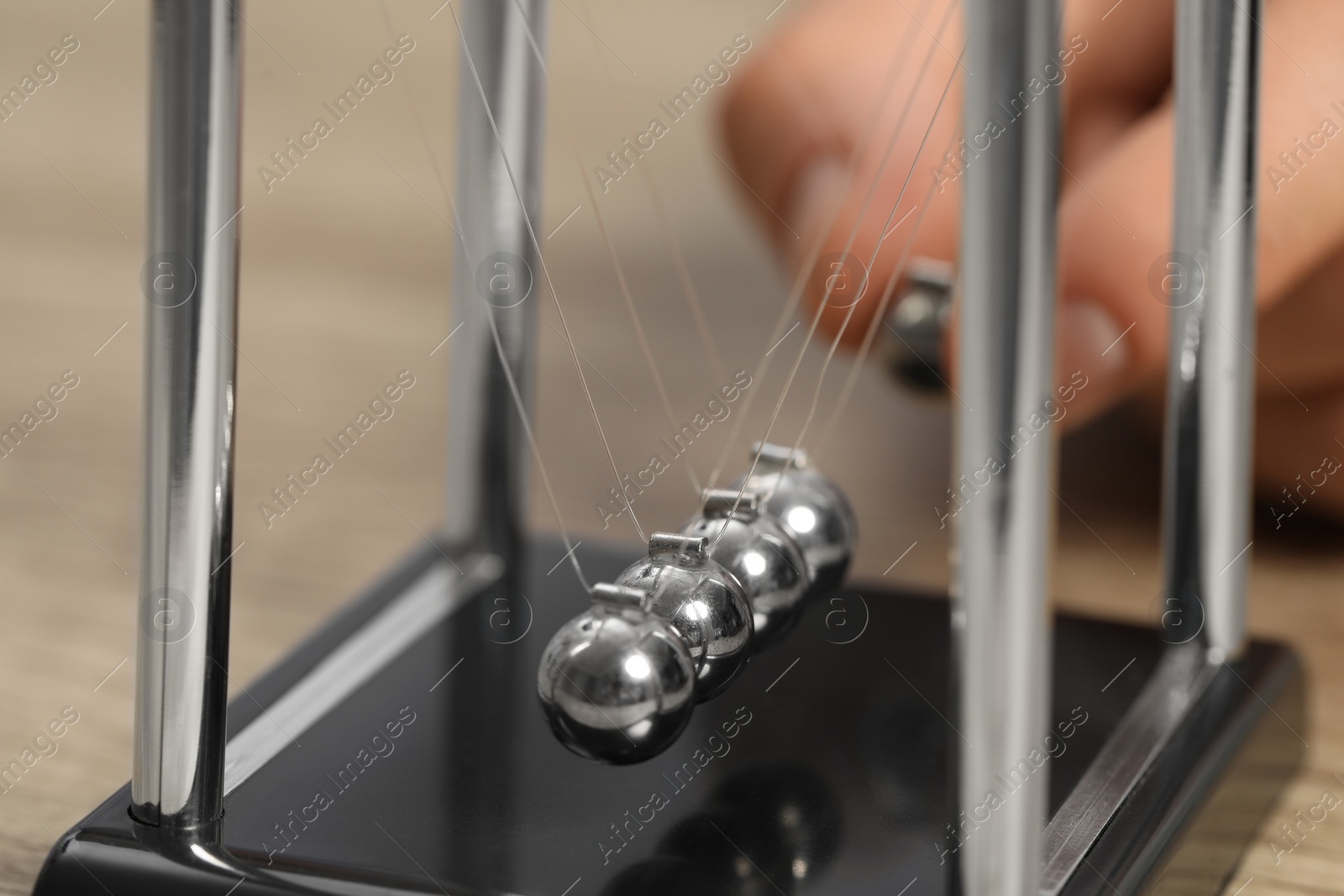 Photo of Man playing with Newton's cradle at table, closeup. Physics law of energy conservation