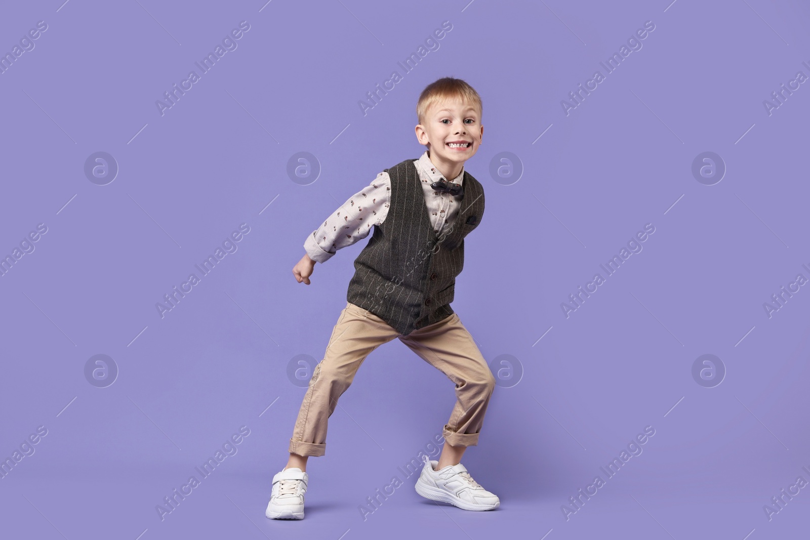 Photo of Happy little boy dancing on violet background. Space for text