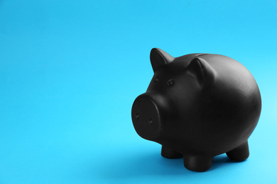 Black piggy bank on blue background. Space for text