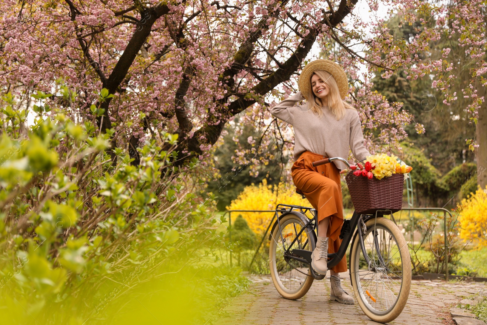 Photo of Beautiful young woman with bicycle and flowers in park on pleasant spring day. Space for text