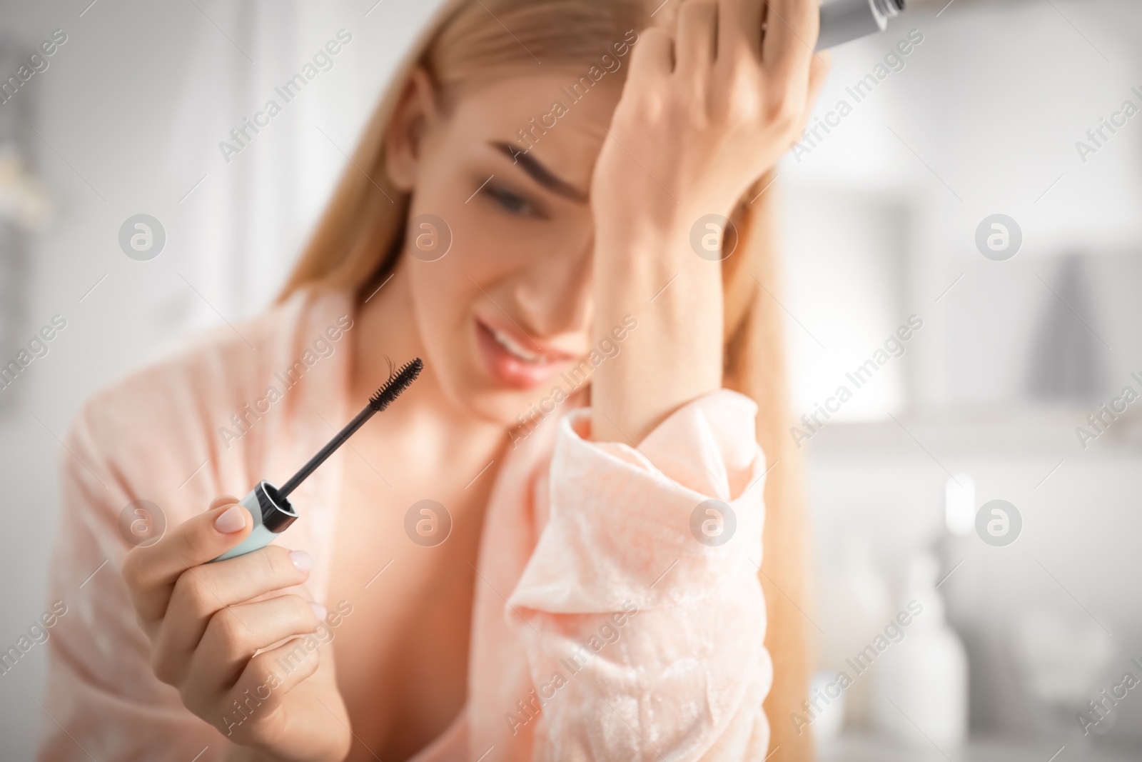 Photo of Young woman holding mascara brush with fallen eyelashes indoors