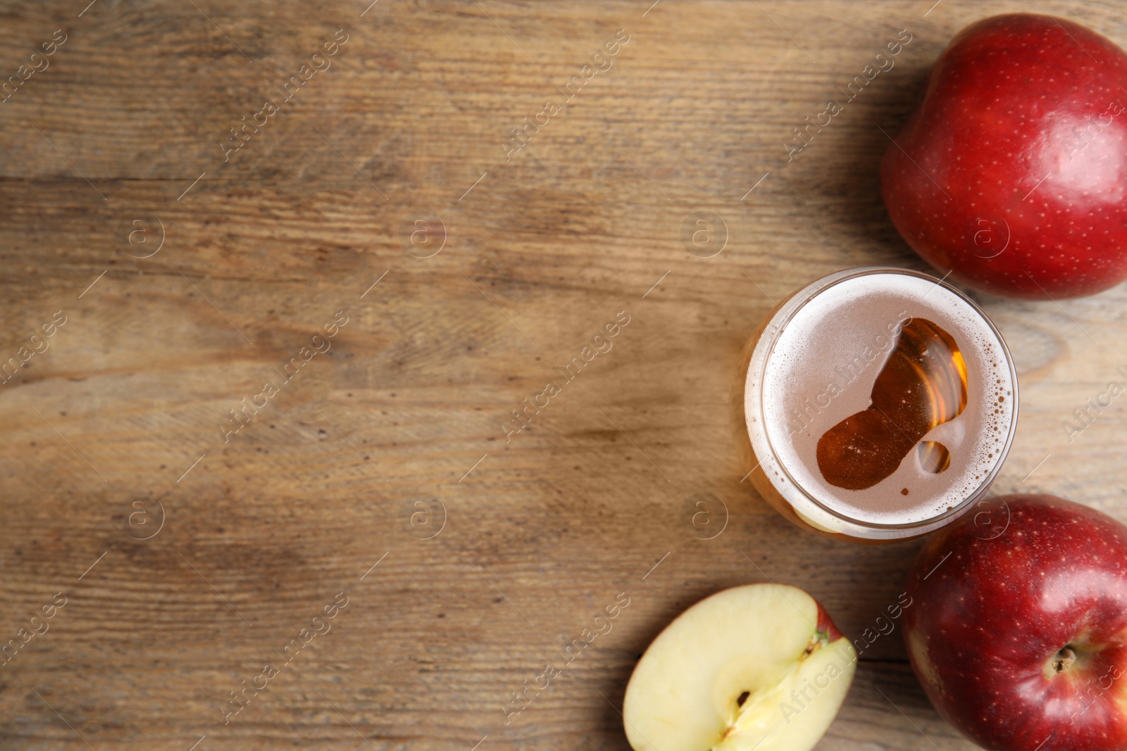 Photo of Glass of delicious cider and ripe red apples on wooden table, flat lay. Space for text