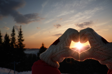 Woman making heart with hands outdoors on sunset, closeup. Winter vacation
