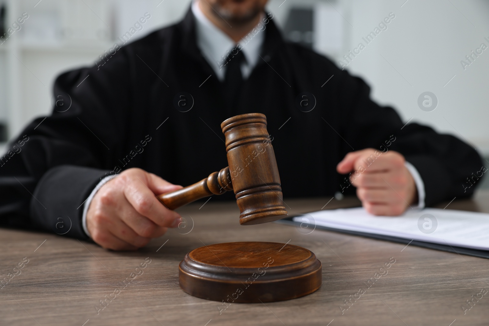 Photo of Judge with gavel and papers sitting at wooden table indoors, closeup