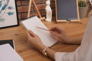 Photo of Woman drawing in sketchbook with pencil at wooden table indoors, closeup