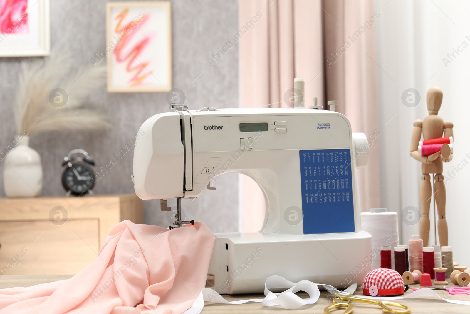 Photo of White sewing machine, cloth, craft accessories and mannequin on wooden table indoors