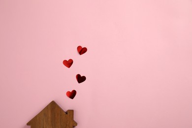 Figure of wooden house and red hearts as smoke from chimney on pink background, flat lay. Space for text