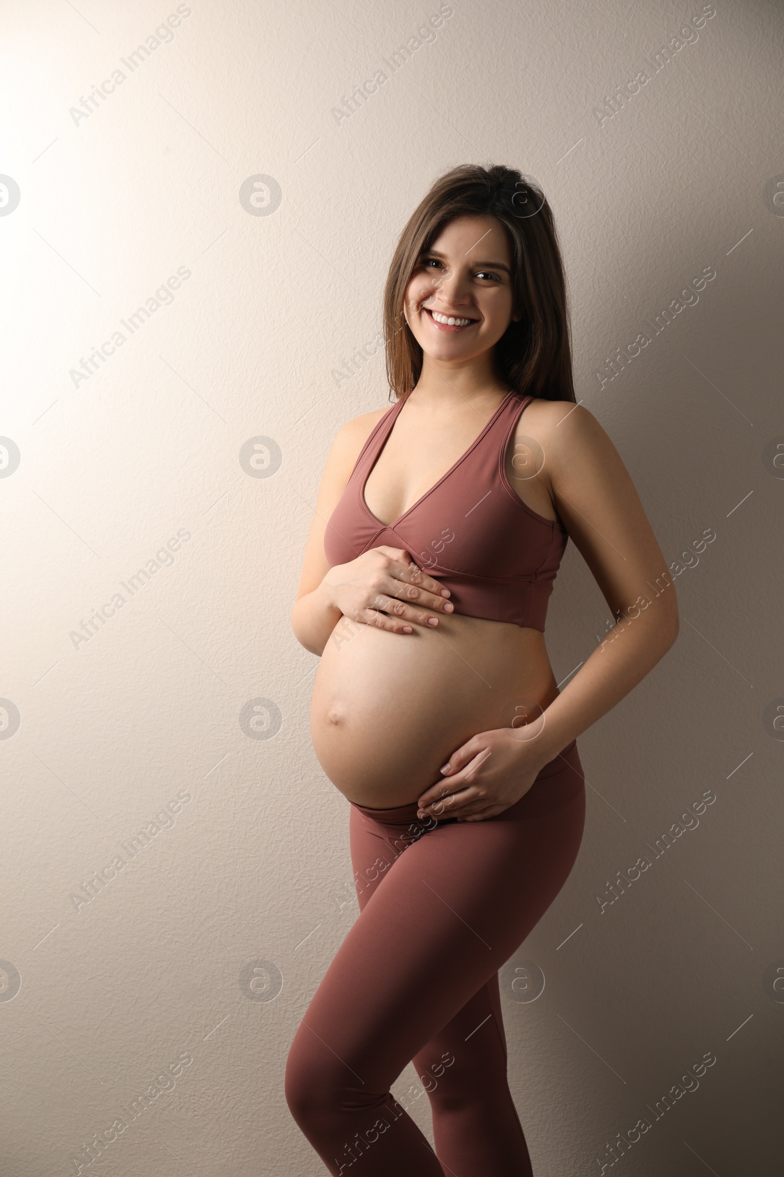 Photo of Pregnant young woman touching belly on beige background