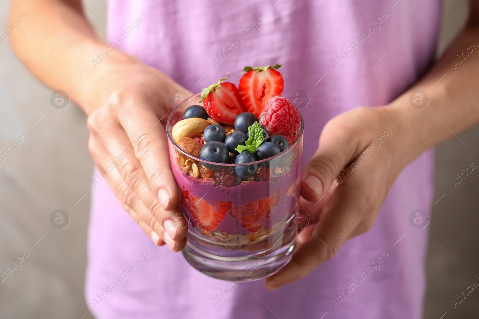 Photo of Woman holding glass of acai dessert with granola and berries, closeup