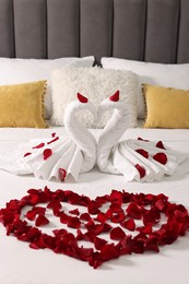 Honeymoon. Swans made with towels and heart of beautiful rose petals on bed in room