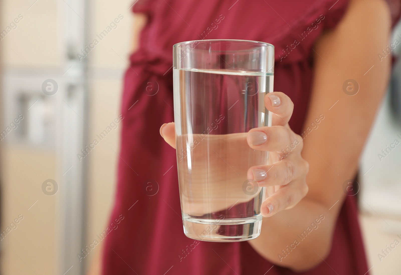 Photo of Woman holding glass with pure water in kitchen, closeup