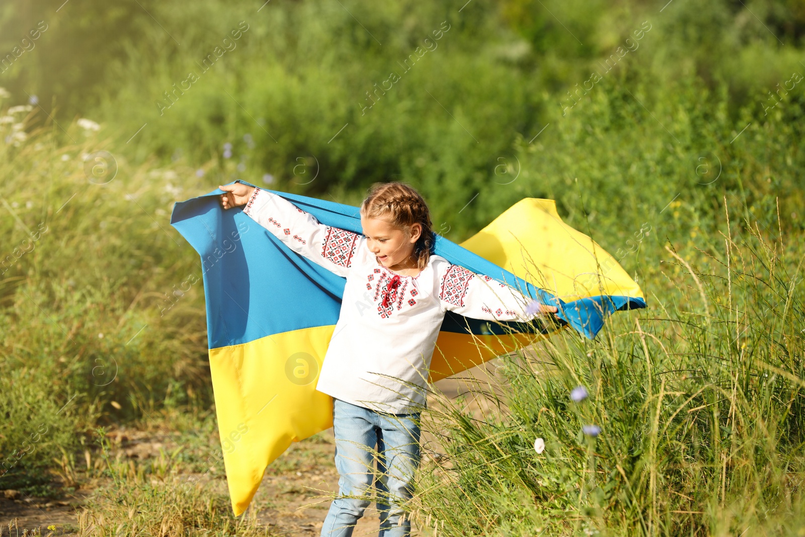 Photo of Little girl in vyshyvanka with flag of Ukraine outdoors