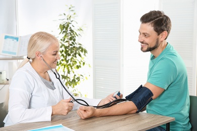 Man visiting doctor in hospital. Measuring blood pressure and checking pulse