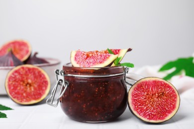 Photo of Glass jar of tasty sweet fig jam and fruits on white tiled table