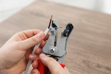 Photo of Professional electrician stripping wiring at wooden table, closeup