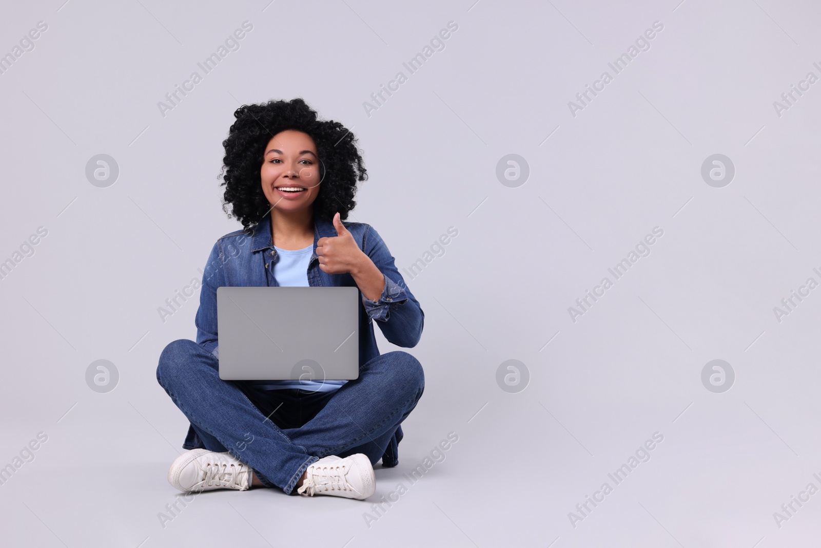 Photo of Happy young woman with laptop showing thumb up on light grey background. Space for text