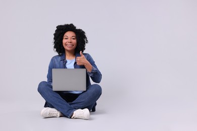 Happy young woman with laptop showing thumb up on light grey background. Space for text