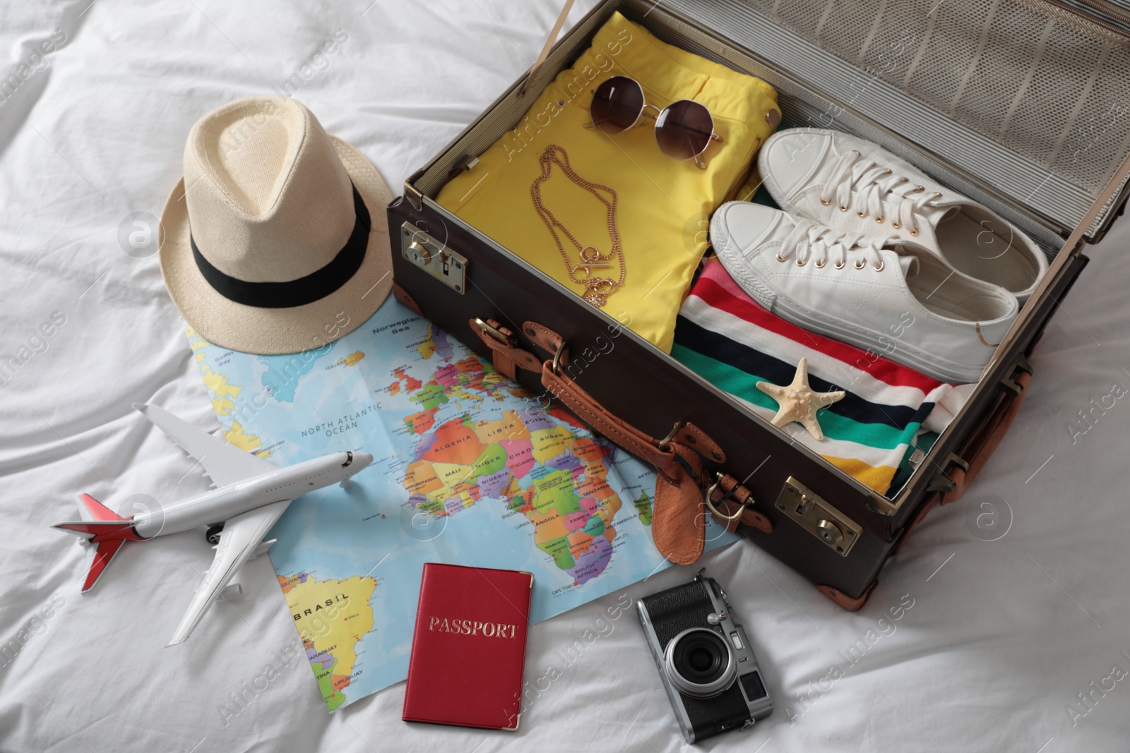 Photo of Packed suitcase and travel accessories on white fabric, above view. Summer vacation