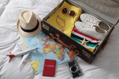 Photo of Packed suitcase and travel accessories on white fabric, above view. Summer vacation