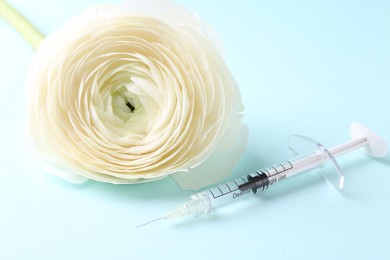 Photo of Cosmetology. Medical syringe and ranunculus flower on light blue background, closeup