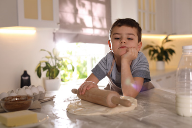 Photo of Cute little boy with dough and rolling pin at table in kitchen. Cooking pastry