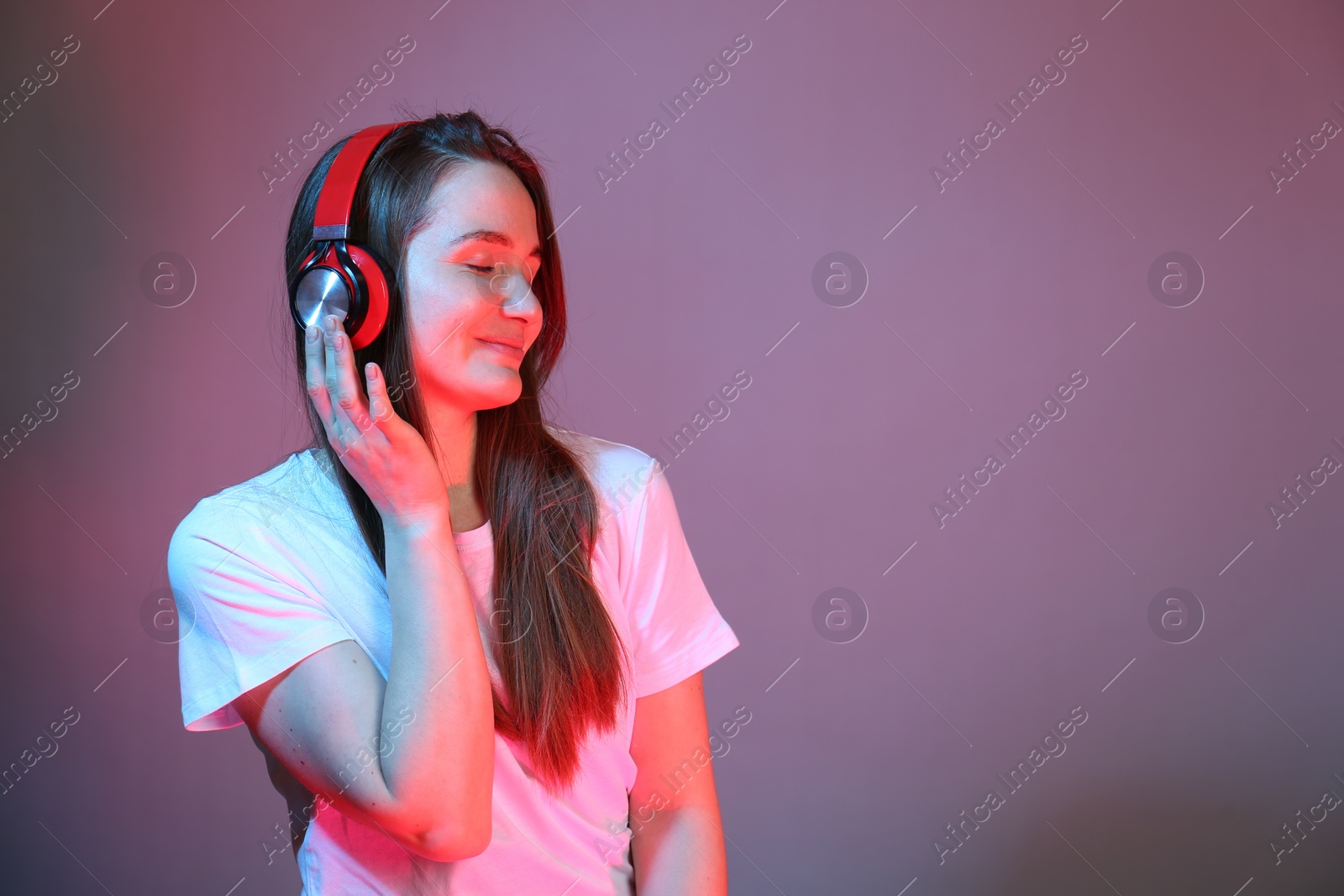 Photo of Portrait of beautiful woman with headphones in neon lights on color background, space for text