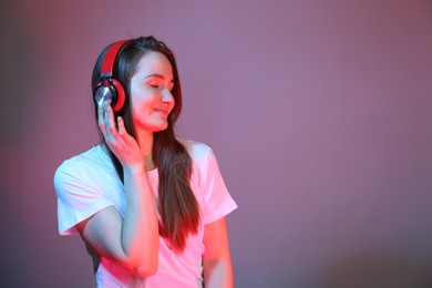 Portrait of beautiful woman with headphones in neon lights on color background, space for text
