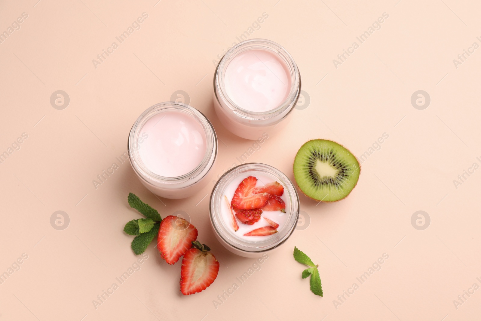 Photo of Jars of fresh yogurt, strawberry and kiwi on light pink background, flat lay