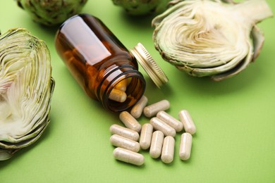 Photo of Bottle with pills and fresh artichokes on light green background, closeup