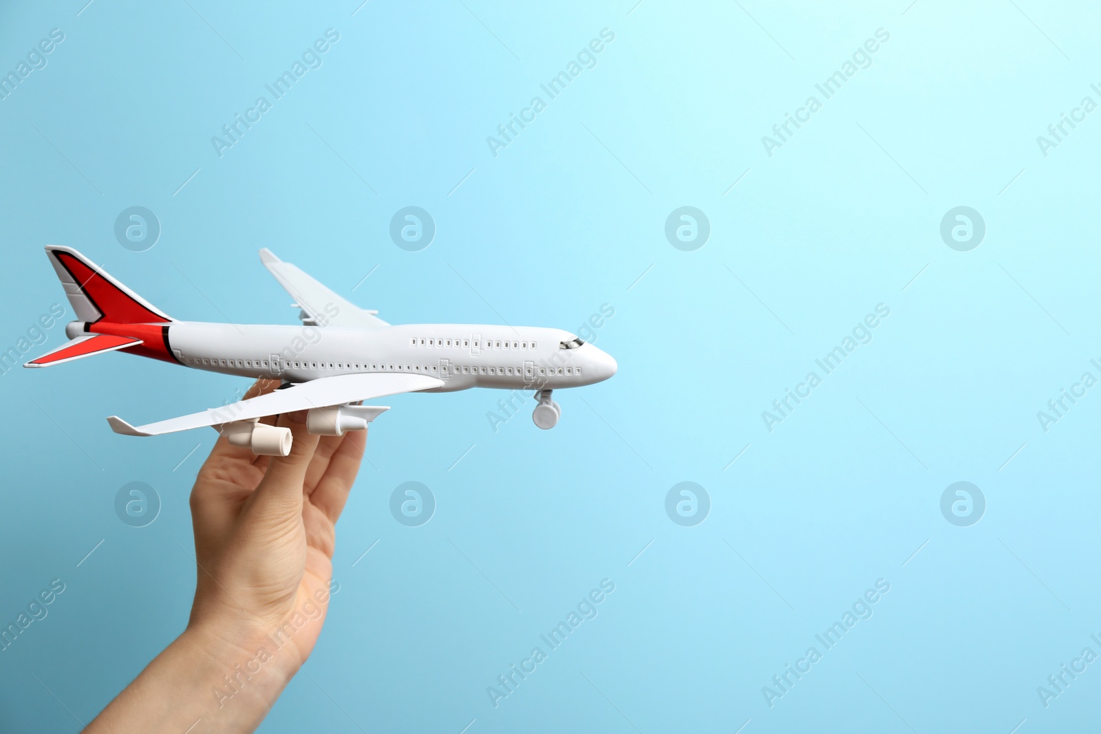 Photo of Woman holding toy airplane on light blue background, closeup. Space for text