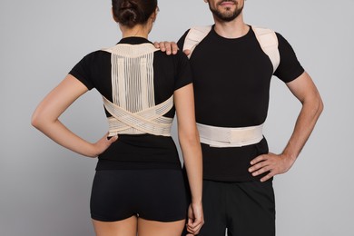 Closeup view of man and woman with orthopedic corsets on grey background