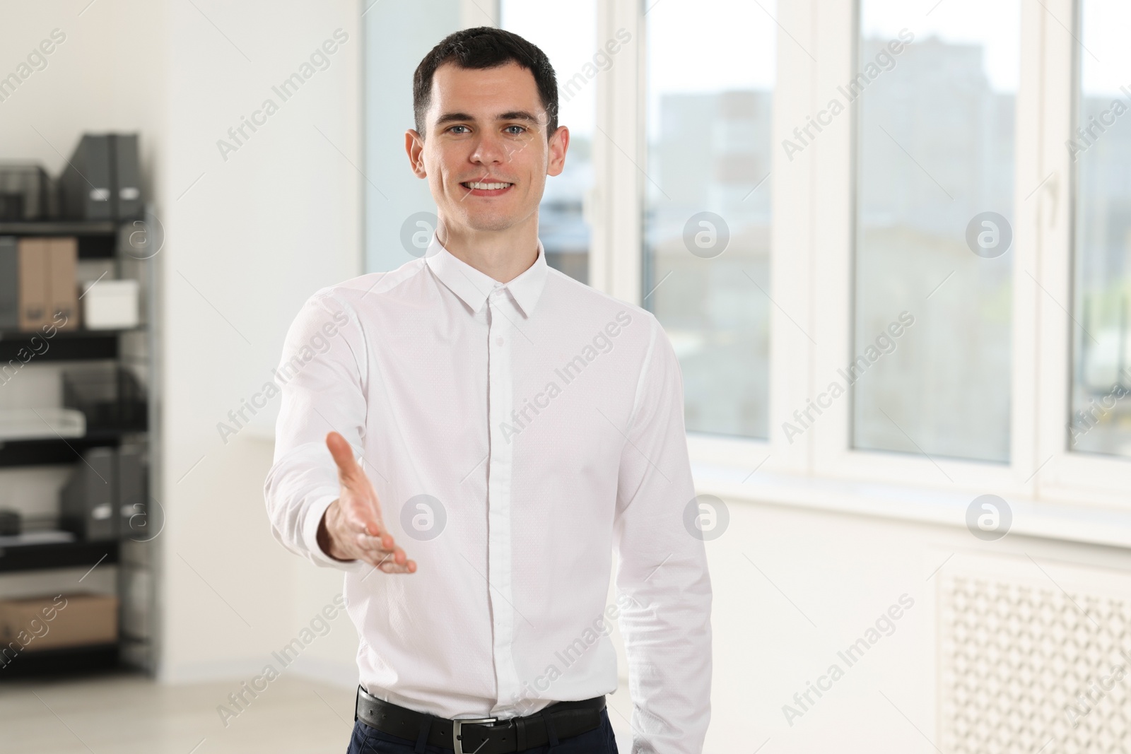 Photo of Happy man welcoming and offering handshake in office, space for text