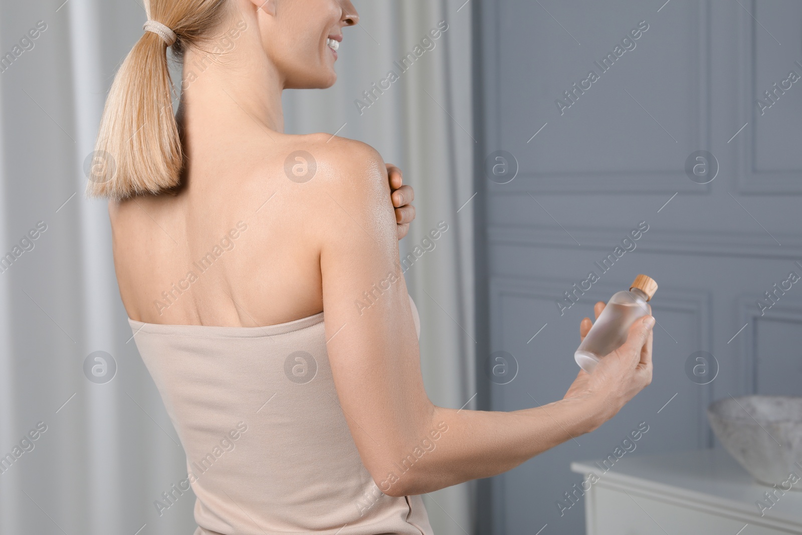 Photo of Woman with bottle of body oil in bathroom, closeup. Space for text