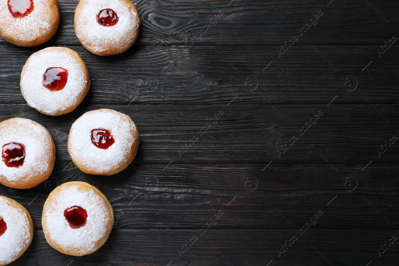 Photo of Hanukkah doughnuts with jelly and sugar powder on black wooden table, flat lay. Space for text