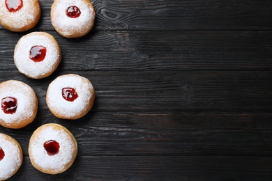 Photo of Hanukkah doughnuts with jelly and sugar powder on black wooden table, flat lay. Space for text